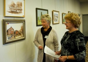 Society President Linda Kale and guest Bette Schmitt view one of Robert Enlow's many landscapes.